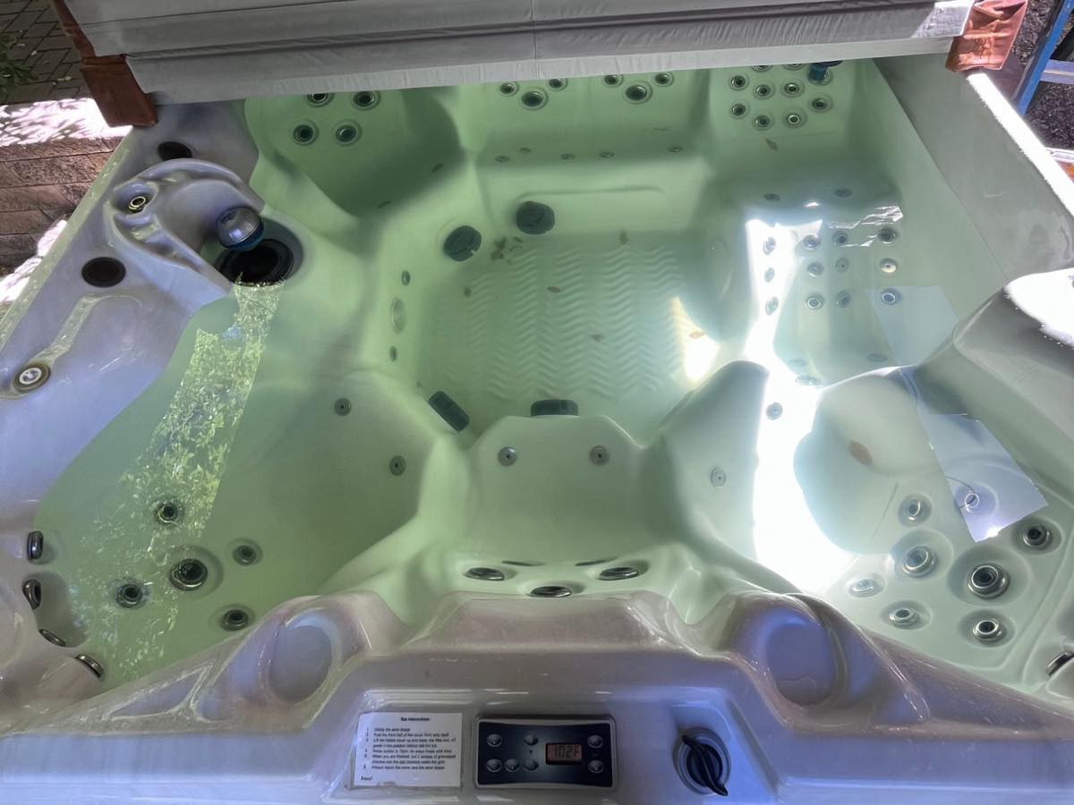 Hot tub with cloudy green-tinted water and floating debris before a regular weekly visit